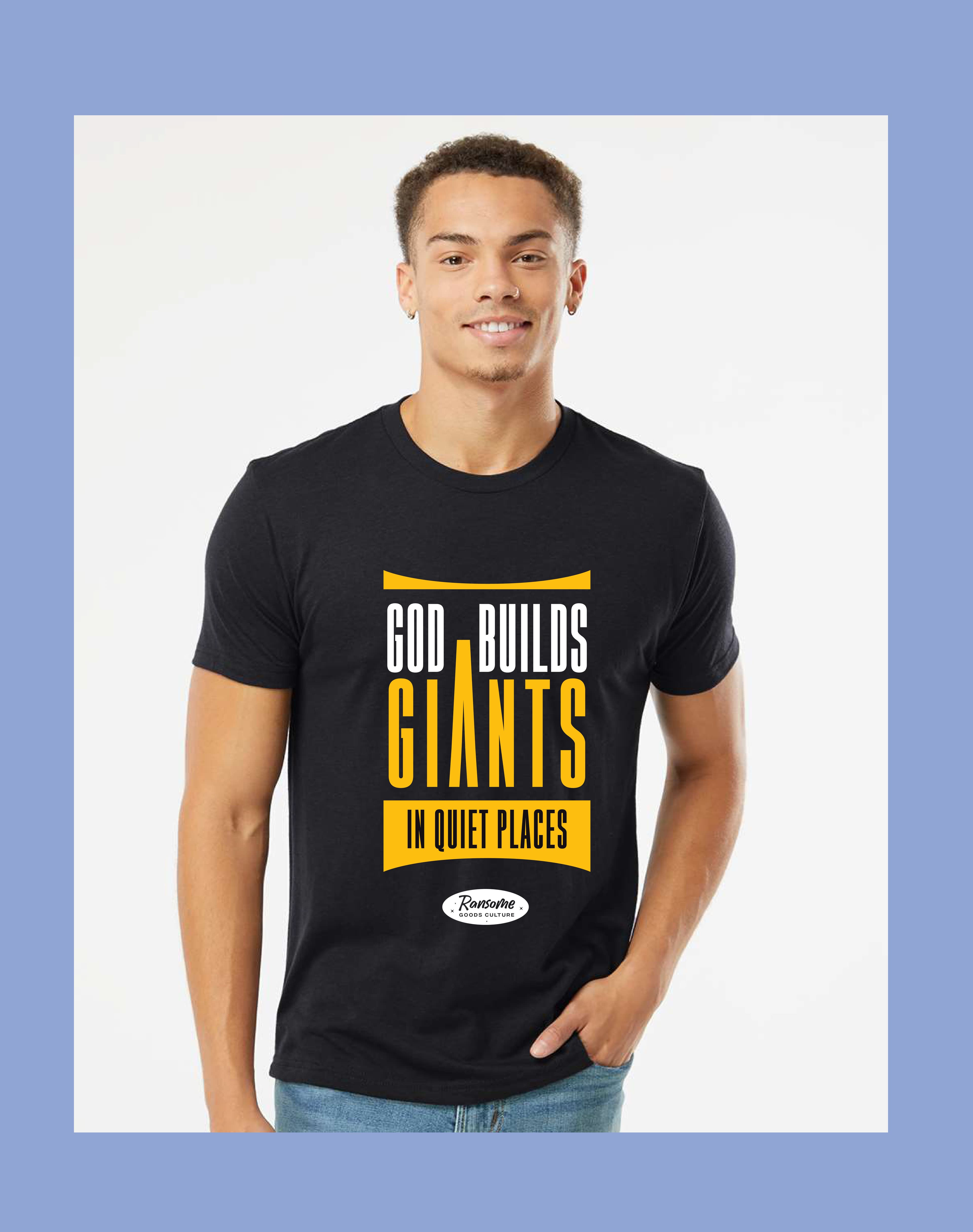 Smiling man wearing a black t-shirt with yellow text 'God Builds Giants in Quiet Places'.