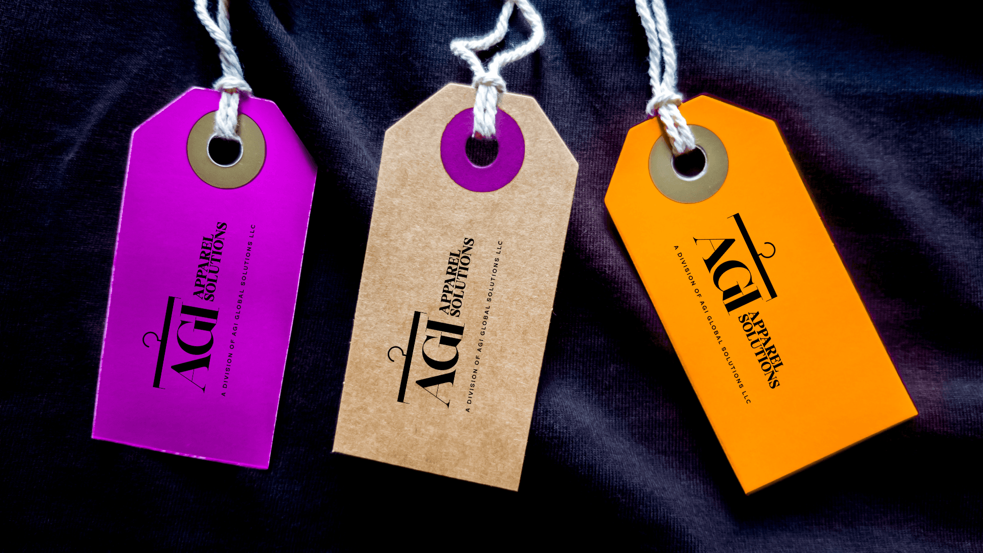 Purple, brown, and orange clothing tags with AGI Apparel Solutions logos on dark fabric.